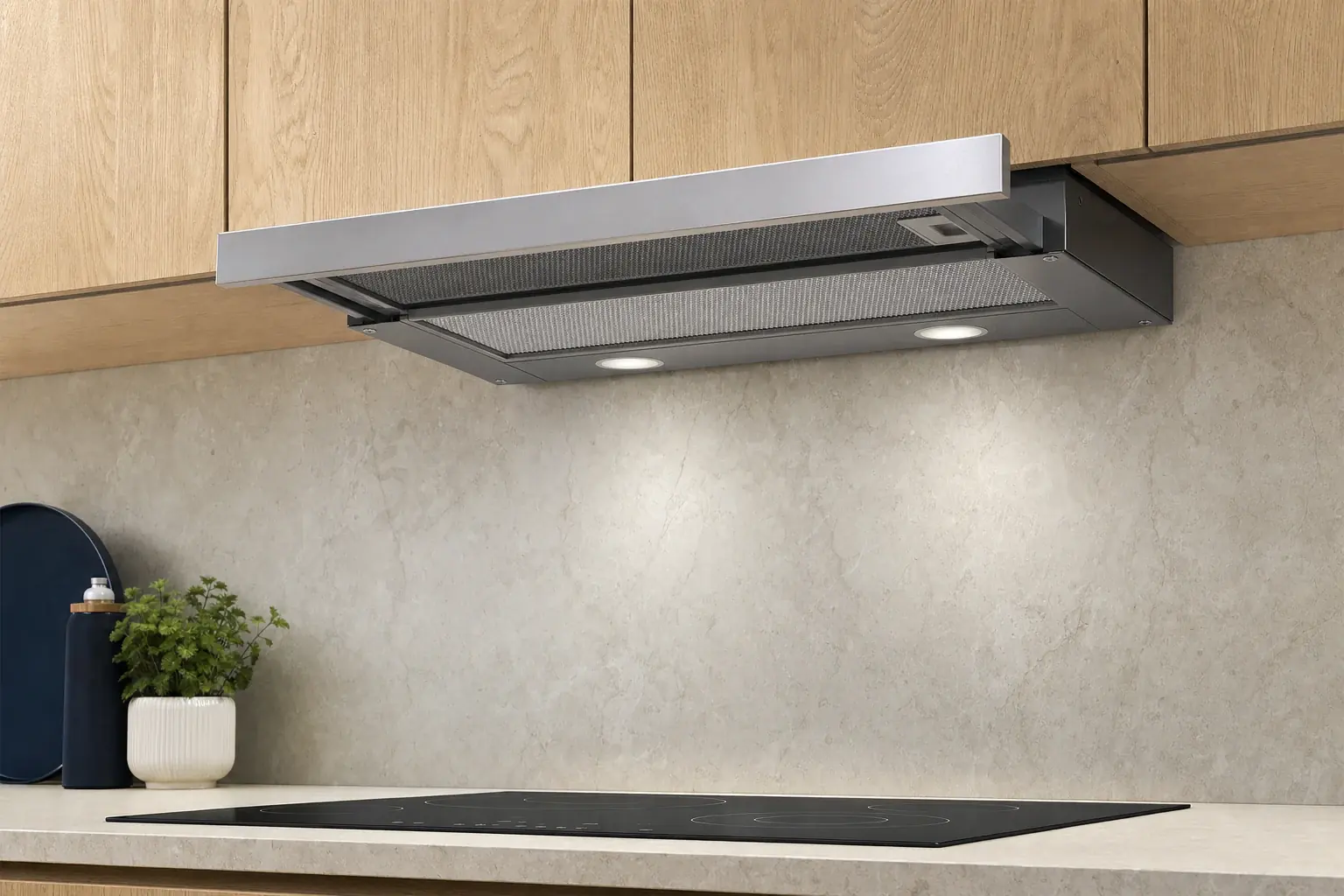 A discreet telescopic built-in kitchen extractor integrated into the underside of an oak upper cabinet, slim stainless front strip pulled slightly forward revealing the mesh filter underneath, above a dark cold hob